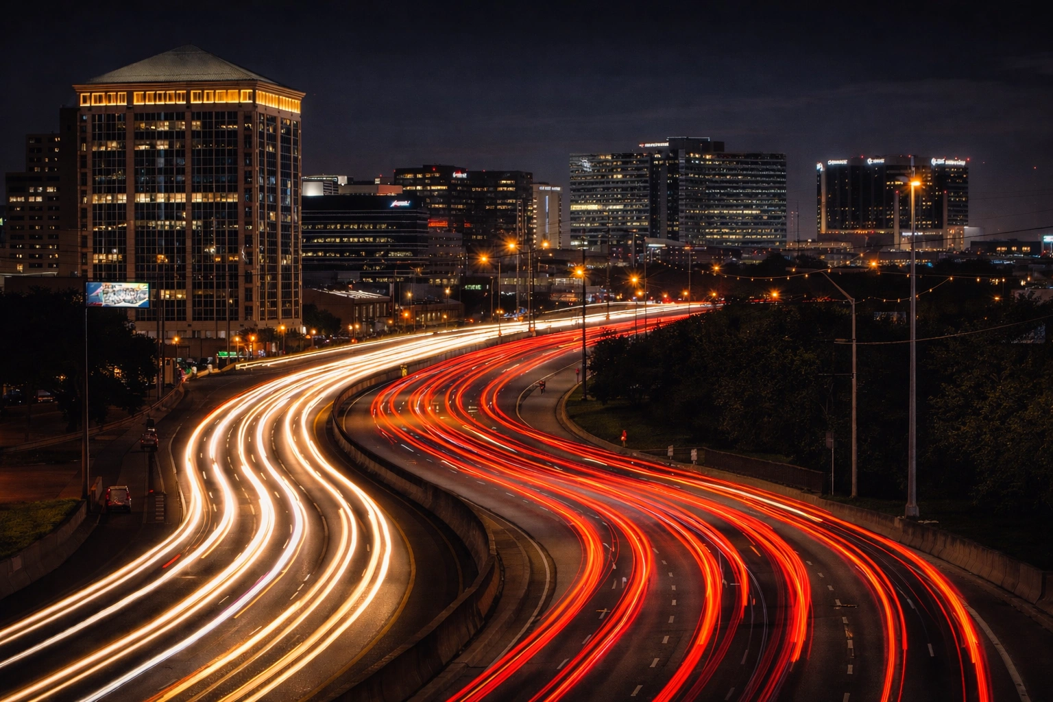 Long exposure of Dallas North Tollway at night through Addison with light trails curving past office towers
